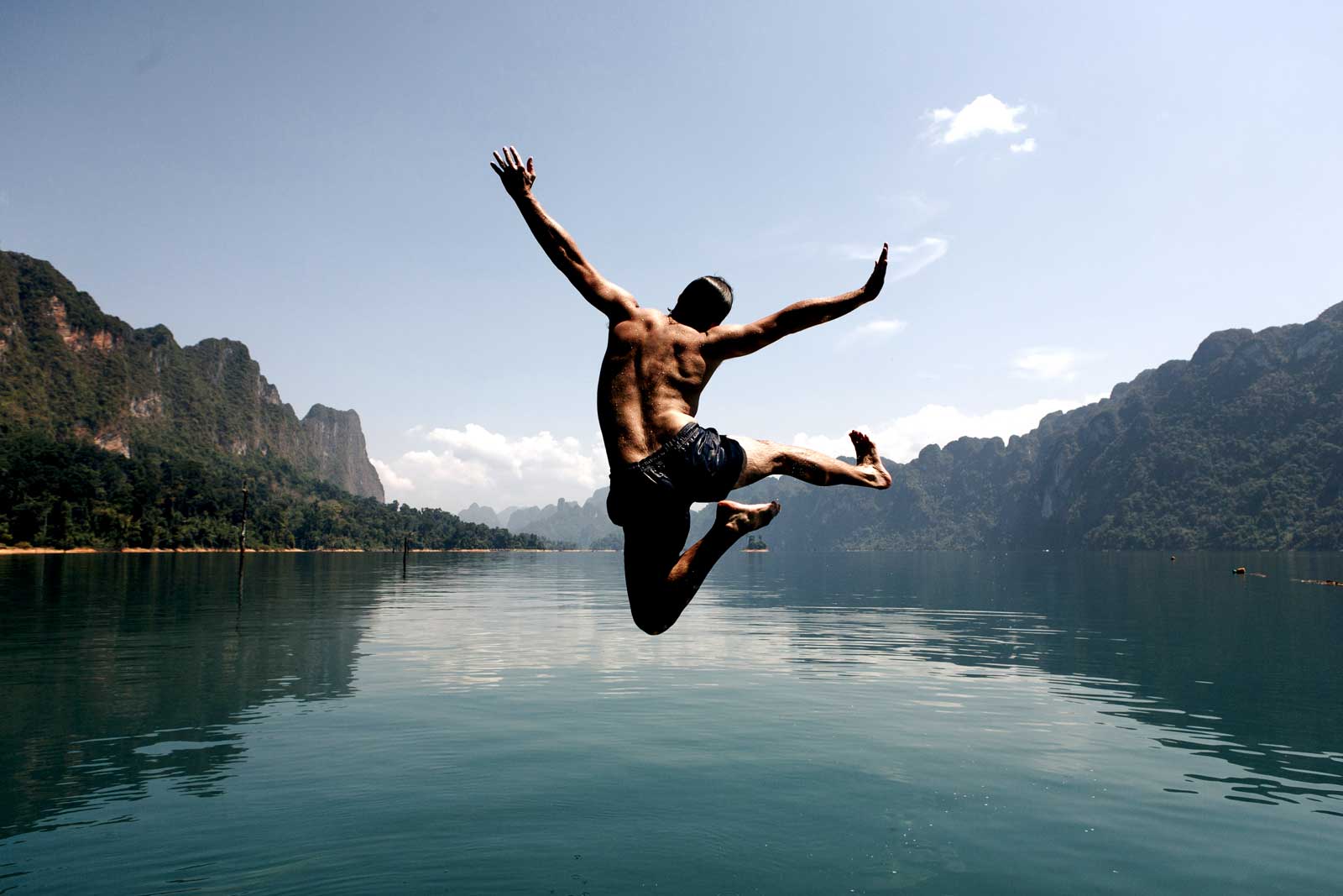 image of man jumping strongly into a beautiful lake